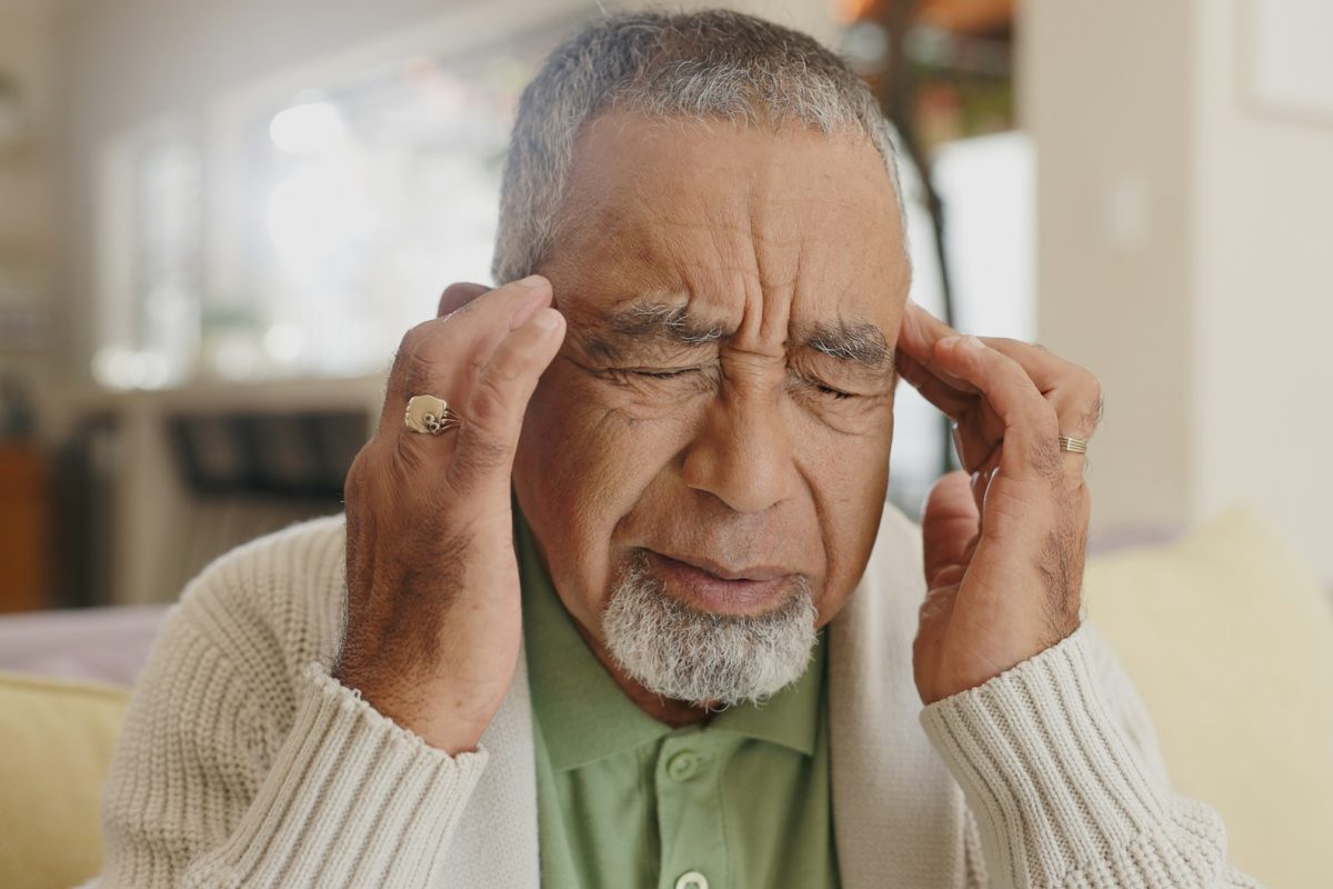 Home, senior man and headache on sofa for stress, emotional conflict and temporal vertigo. Living r